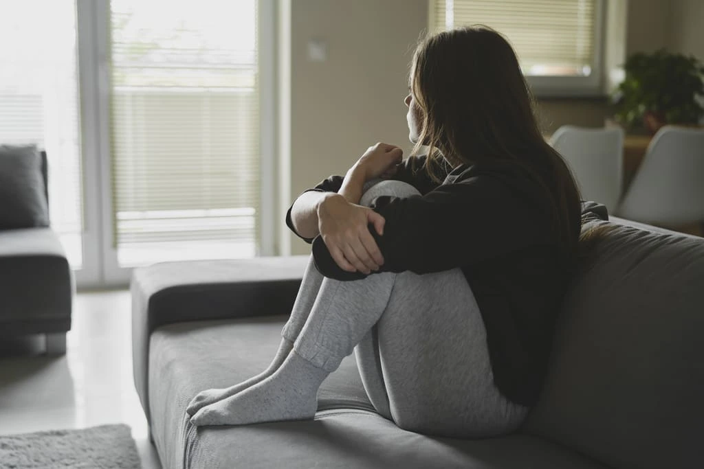 depressed woman sitting on a sofa holding her legs