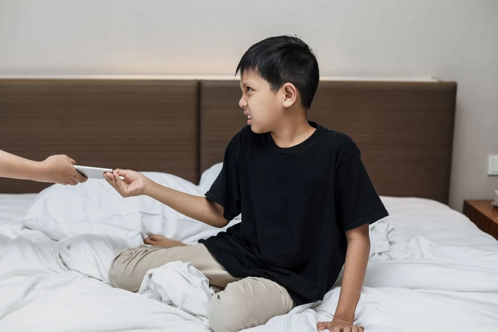 kid sitting in bed refusing to give back the cell phone