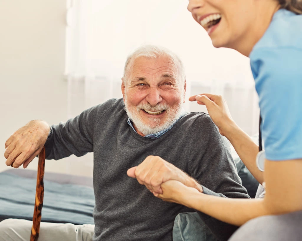 senior person laughing and holding the hand of a caregiver