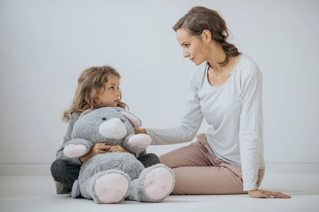 A boy holding a stuffed animal sitting with a therapist